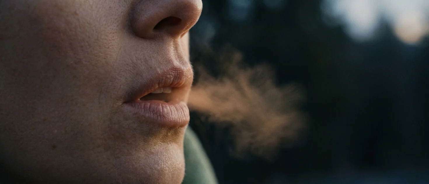 Close-up of parted lips mid-exhale with a soft mist of breath visible in cool air, representing the physiological sigh breathing technique